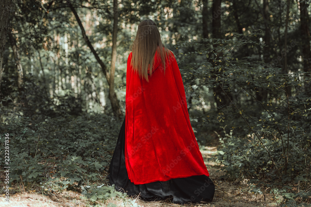 back view of mystic woman in red cloak in forest