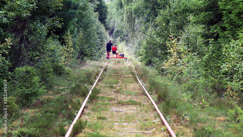 Boy and a girl are flying through the nature on a trolley. They are cycling in Sweden. Vehicle on a railroad.