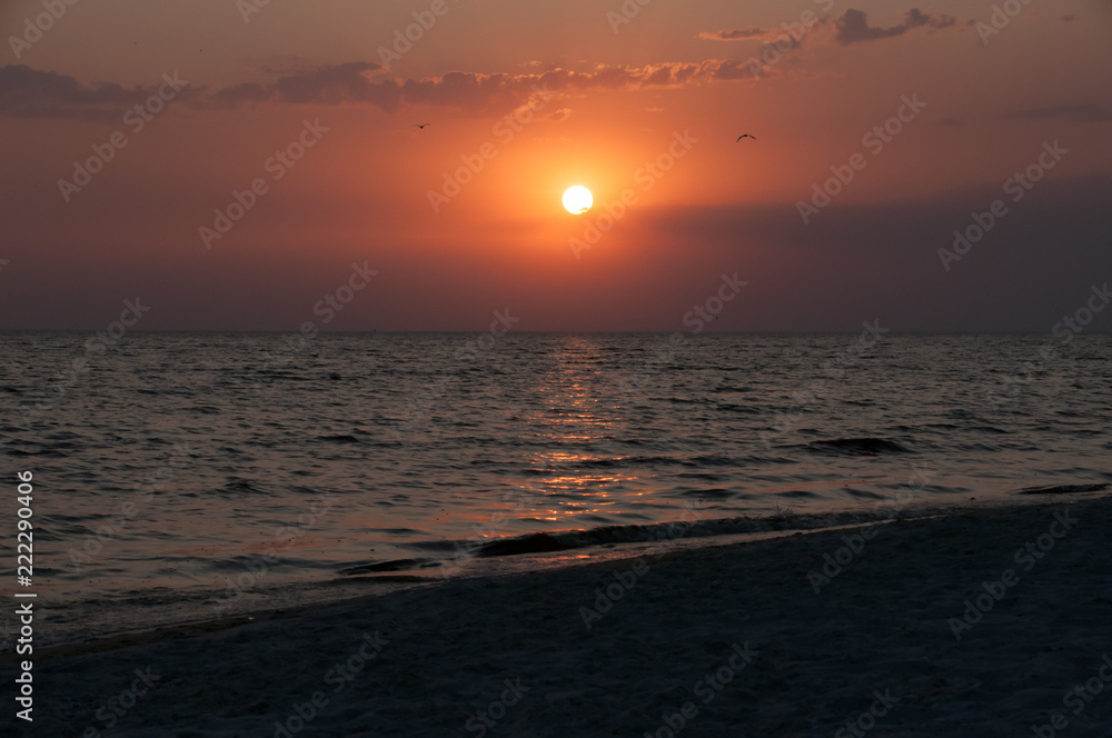 Golden natural sea sunset view of jetty or small bridge at horizon with people silhouette and orange sky landscape. Sunset or sunrise reflection in nature with sun in clouds above black sea scenery.