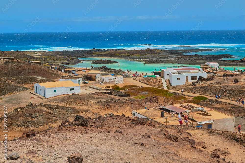 Nice view of white fisherman houses and people bathing and sunbathing on the blue water beach in Isla de Lobos, Fuerteventura, Canary Islands, Spain