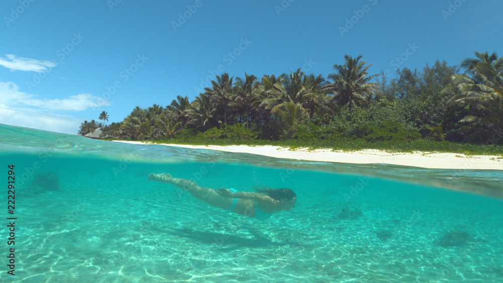 HALF UNDERWATER: Young woman dives in the glimmering turquoise ocean water.