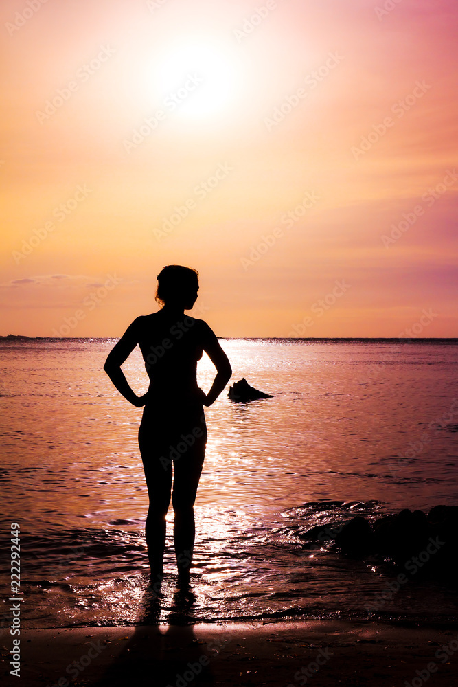 Silhouette of a beautiful woman standing on the beach at sunset looking at the pacific ocean in summer in Puerto Rico