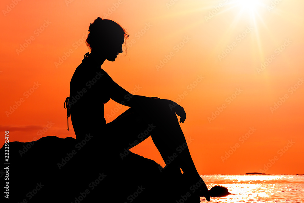 Silhouette of a beautiful woman sitting on a rock at sunset looking at the pacific ocean in summer in Puerto Rico