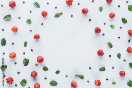 top view of round frame made of ripe strawberries with mint leaves and coffee beans on white surface