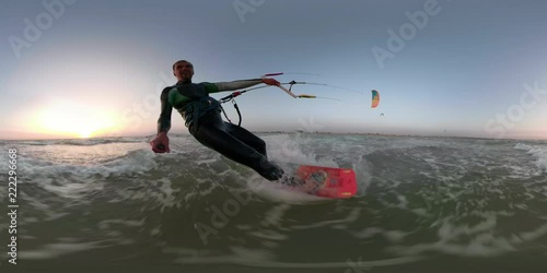 A man on a red wakeboard is engaged in kitesurfing and is holding a selfie stick photo