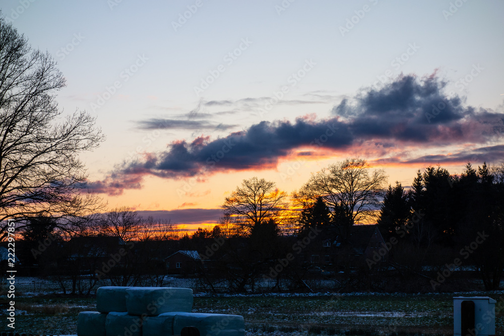 Sonnenuntergang in einer Landschaft mit Bäumen und Feldern am Abend mit Wolken