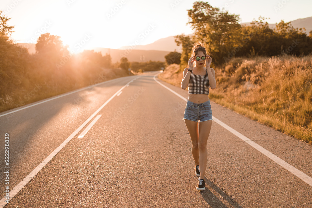 Young girl with hair bun and denim shorts dancing walking and smiling on the edge of the roadway in a sunset of summer Young girl with hair bun and denim shorts dancing walking and smiling on the edge of the roadway in a sunset of summer