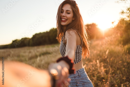 Front view of young brunette girl with long hair taking the hand of photographer sunset background