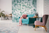 Chair and turquoise sofa in green living room interior with leaves wallpaper and table. Real photo