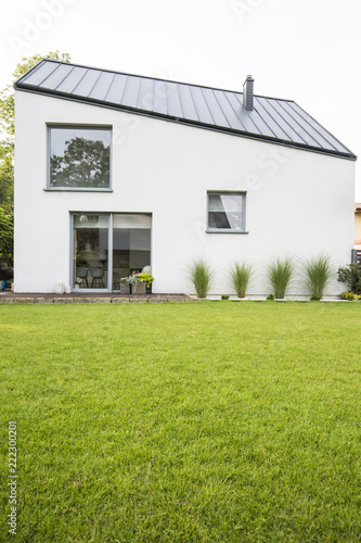 Green lawn in the backyard of a luxurious house with wooden terrace in the summer. Real photo
