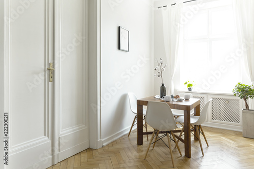 Quadro su tela A small wooden dining table with chairs in a sunny room interior with white walls, double door and a window