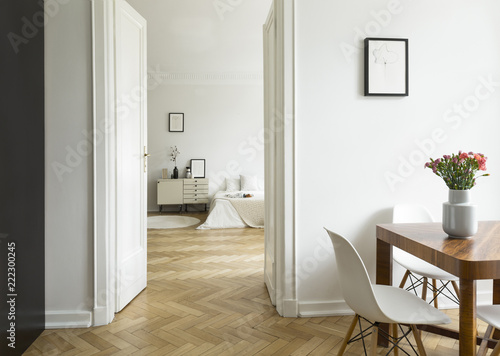 A long distance view from a dining room into a bedroom in a high ceiling flat. Monochromatic white interior with herringbone parquet. Real photo.