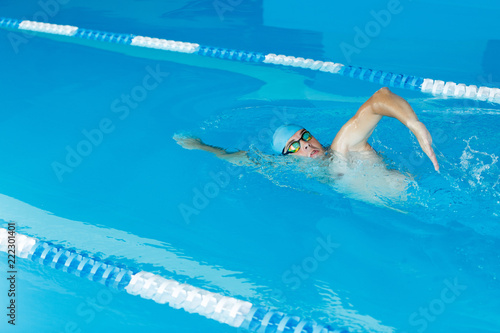 Photo of young sports man in blue cap swimming in pool