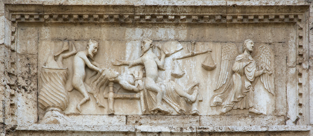 Angels and demons on medieval bas-relief, from the facade of Saint Peter church, Spoleto, Italy.