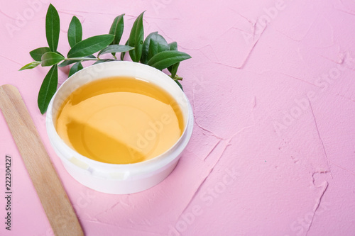 Plastic bowl with sugaring paste and stick on color background