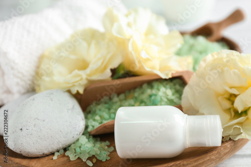 Bottle with cream, sea salt and spa stones on wooden tray, closeup