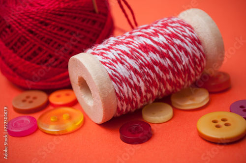 closeup of buttons and bobbins of cotton yarn on orange background