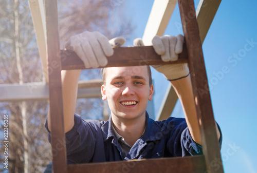 A smiling young man in gloves and work clothes is building a roof