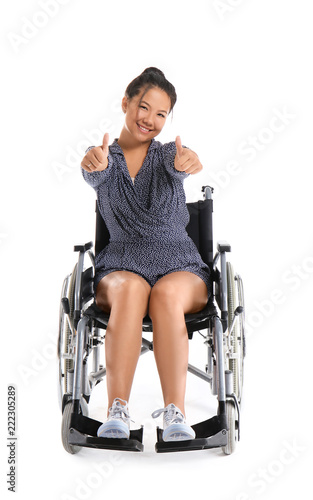 Asian woman in wheelchair showing thumb-ups gesture on white background