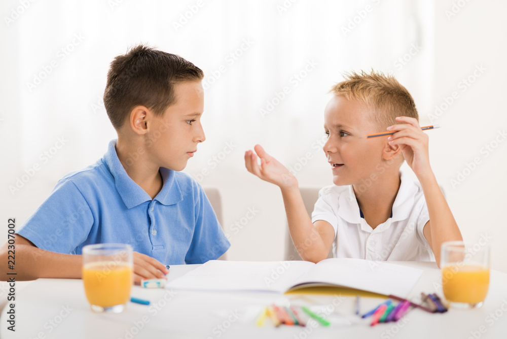 Two smiling little boys drawing in the notebook and talking to each other. Two smiling little boys drawing in the notebook and talking to each other.
