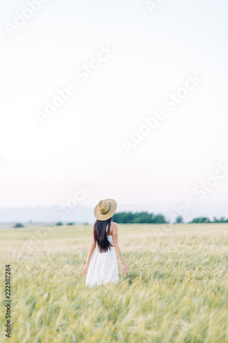 Girl walking on the field, in a hat and summer dress. Smiling and laughing, beautiful sunset in the forest and in nature. Happy traveler, lifestyle.