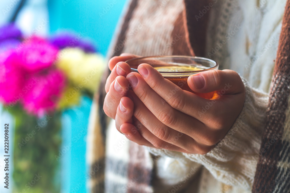 Obraz premium Tea drinking. The woman in a knitted, white pullover and in a warm plaid holds a cup of hot tea with lemon in her hands. Cozy weekends, winter drinks. Ceylon, Chinese tea