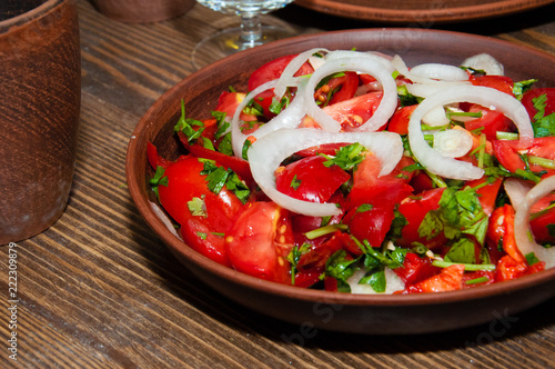 Salad of tomatoes, cucumbers, peppers, onions and greens dressed with olive, sunflower or corn oil in earthenware, wine glass, clay mug photo