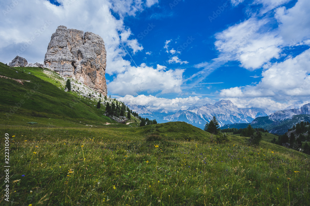 Famous Dolomiti landmark, Cinque Torri. Rock towers in green meadows and pastures of Dolomiti, blue sky with dramatic clouds. Trekking, hiking and climbing area. Alpine landscape.