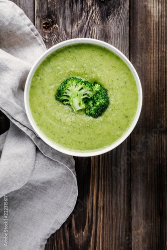Homemade broccoli cream soup in white bowl with toasts on wooden background