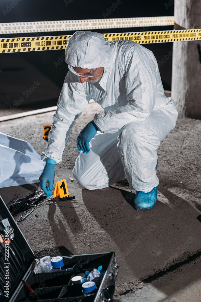 male criminologist in protective suit and latex gloves collecting evidence at crime scene with corpse male criminologist in protective suit and latex gloves collecting evidence at crime scene with corpse