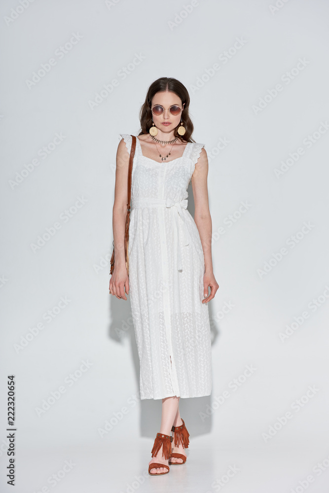 full length view of attractive stylish woman in white dress and sunglasses looking at camera on grey full length view of attractive stylish woman in white dress and sunglasses looking at camera on grey