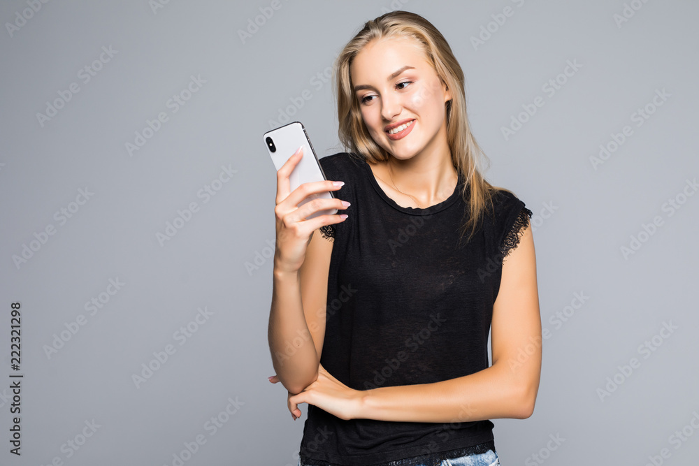 Surfing the net. Attractive young woman smiling and using her smart phone while standing against grey background Surfing the net. Attractive young woman smiling and using her smart phone while standing against grey background