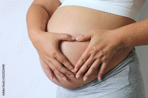 Wallpaper Mural Happy pregnant women hand shows symbol heart shape of love on her belly on white background Torontodigital.ca
