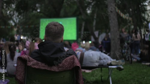 man in an armchair watching a movie outdoors in a park
