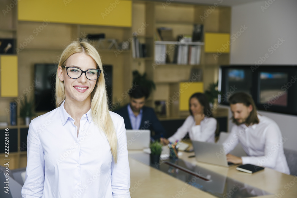 Young businesswoman standing in the office and other young business people working in the background