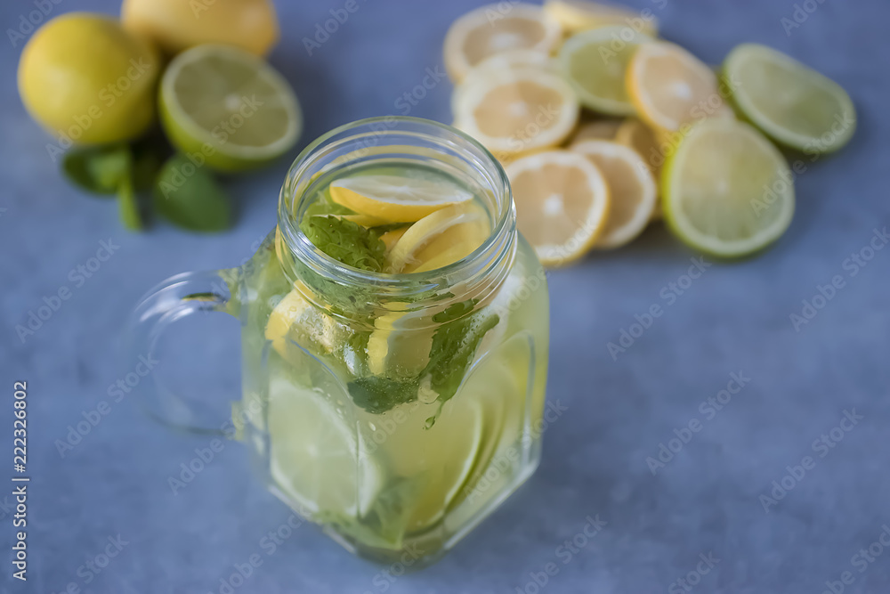 Refreshing lemonade with lemon and lime slices and mint leaves in a glass mug on a gray background. Soft focus. Refreshing lemonade with lemon and lime slices and mint leaves in a glass mug on a gray background. Soft focus.