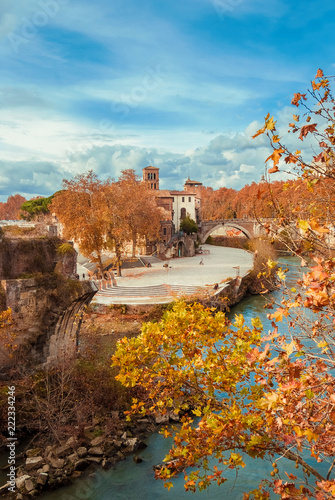 Autumn and foliage in Rome. Red and yellow leaves near Tiber Island with two ancient bridges and beautiful sky, in the city historic center