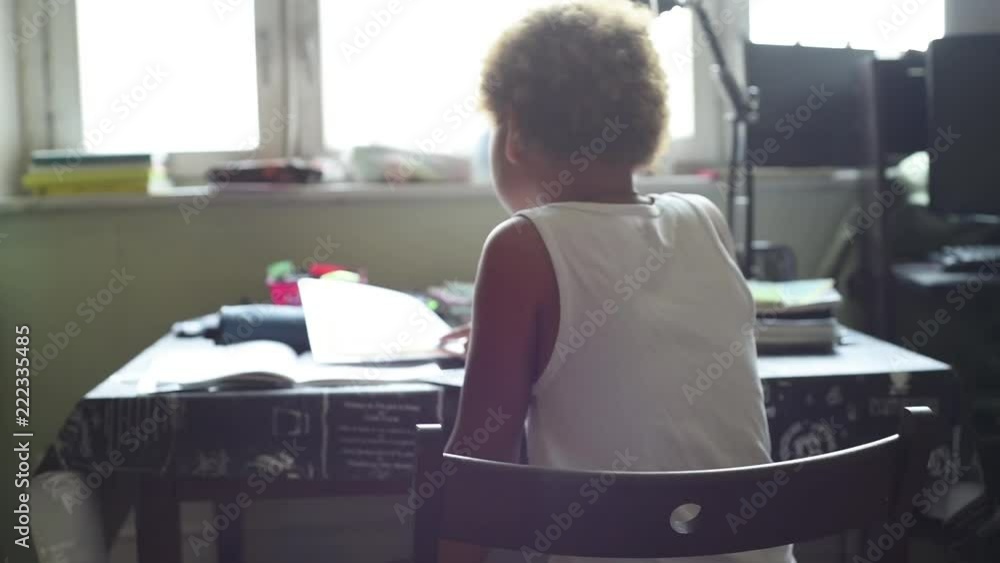 Schoolboy doing homework in his room in the home. Cute african american boy sitting at the table and thinking and writing in his notes. Home education for kids. Boy learning something from his book. Schoolboy doing homework in his room in the home. Cute african american boy sitting at the table and thinking and writing in his notes. Home education for kids. Boy learning something from his book.