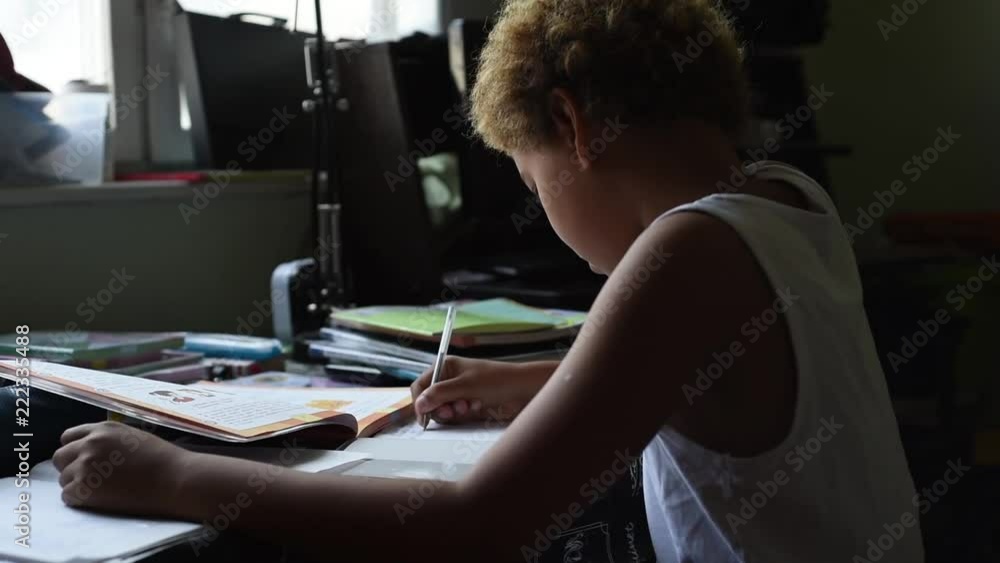 Schoolboy doing homework in his room in the home. Cute african american boy sitting at the table and thinking and writing in his notes. Home education for kids. Boy learning something from his book. Schoolboy doing homework in his room in the home. Cute african american boy sitting at the table and thinking and writing in his notes. Home education for kids. Boy learning something from his book.