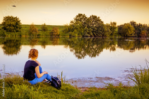 The girl is sitting by the river in the evening and admiring nature_