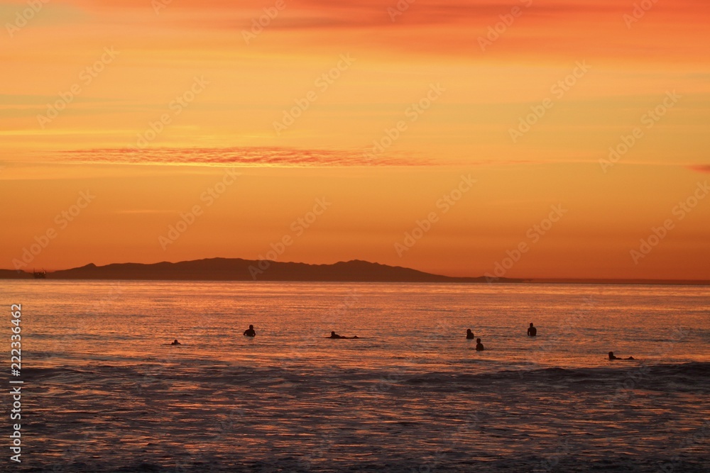 silhouettes of surfers waiting for waves during orange ocean sunset