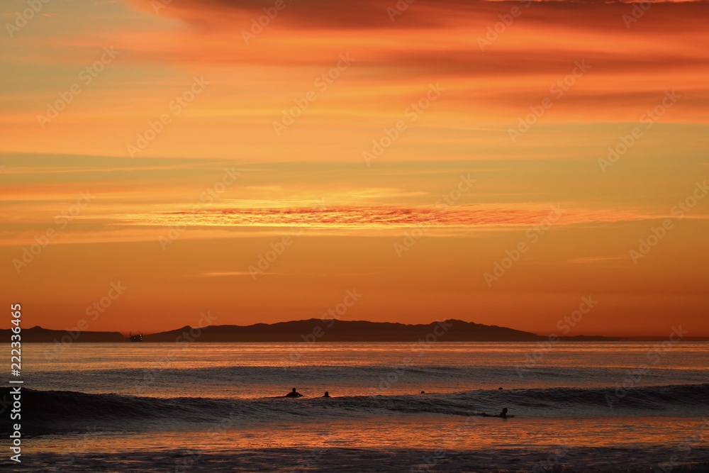 silhouettes of surfers waiting for waves during orange ocean sunset