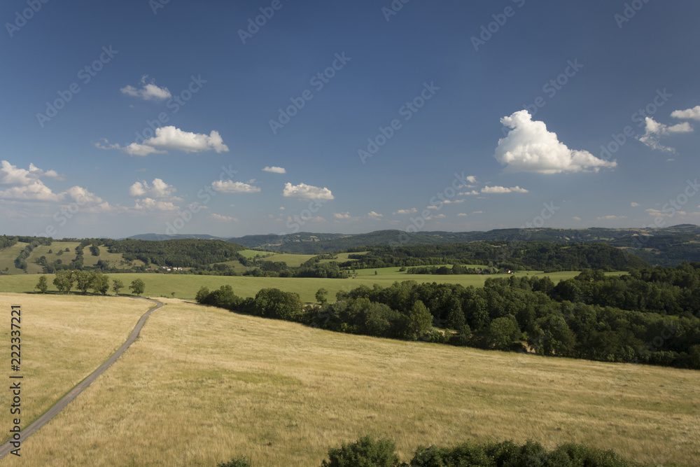 The landscape with meadow, forest, trees, hills and clear blue sky with clouds.