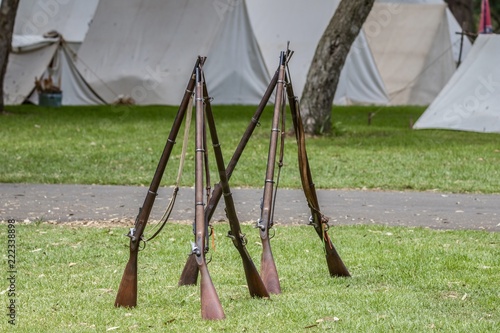 Prop civil war era muskets standing on the grass in front of tents photo