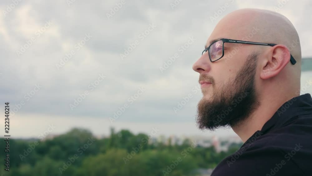 A man with a beard wearing black glasses looks into the distance. Close-up shot. Soft focus A man with a beard wearing black glasses looks into the distance. Close-up shot. Soft focus