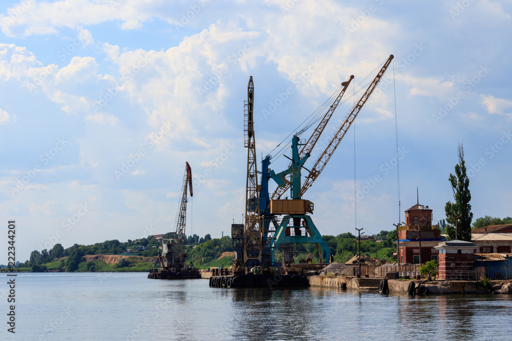 Heavy cranes in cargo port on the riverbank