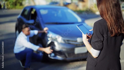 Insurance concept. Female insurance agent inspects damage to a man's car and makes notes on a tablet computer, during discussion with man. Woman with digital tablet inspecting broken car. 4K UHD.