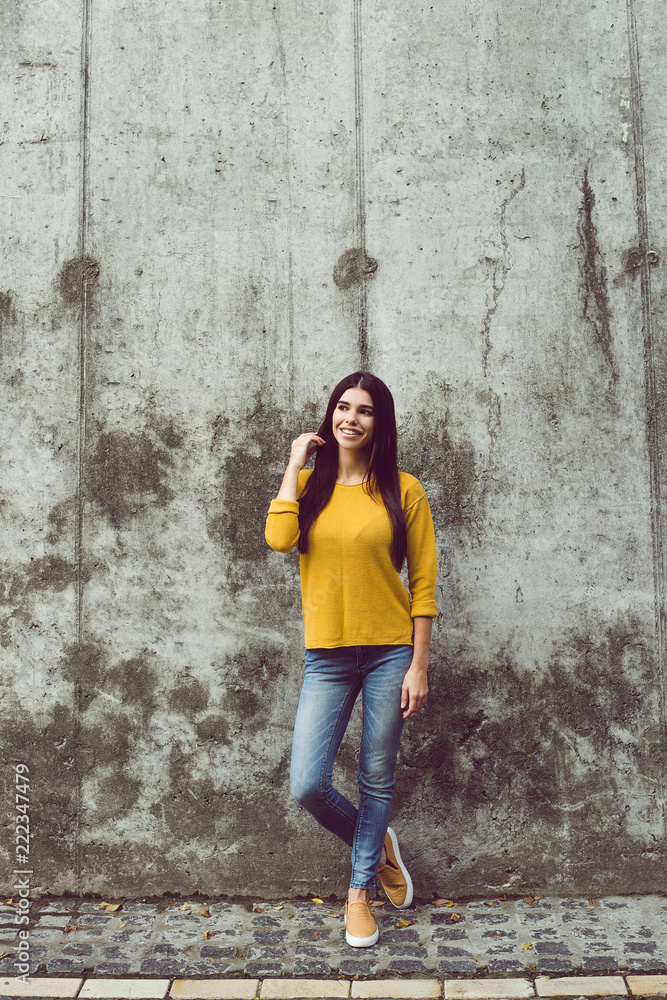 Casual beauty. Full length of beautiful young woman looking at camera with smile while standing against concrete background outdoors 