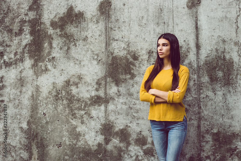 Pensive beauty. Beautiful young woman looking away while standing against concrete background outdoors 