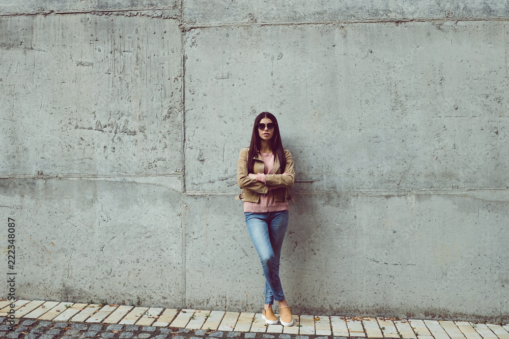 Casual and calm. Full length of beautiful young woman looking at camera while standing against concrete background outdoors 